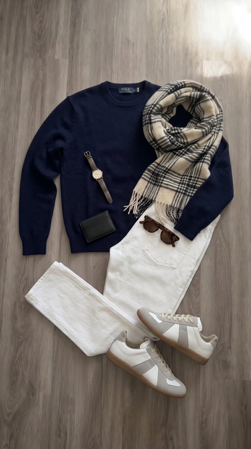 Flat-lay: navy sweater, plaid scarf and white jeans with sunglasses on wood floor